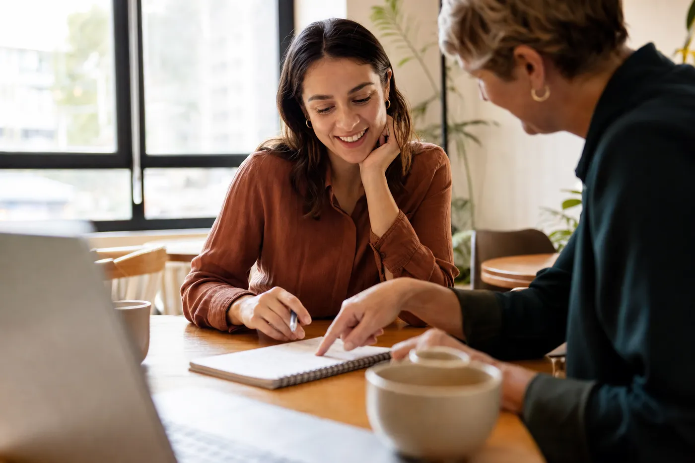 A job seeker smiles as a mentor offers advice over a resume draft in a sunlit workspace.