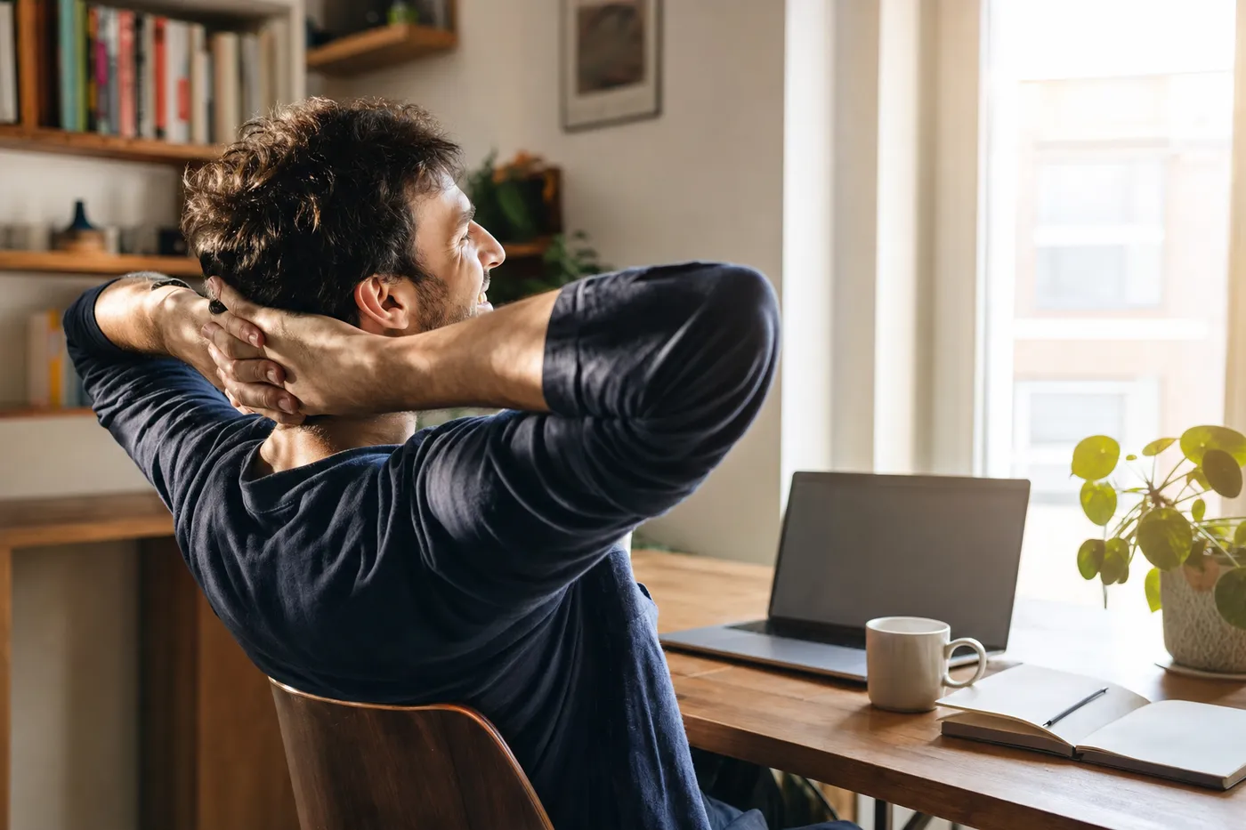 A young man smiling with relief at his laptop in a sunlit room, representing a stress-free resume building experience.