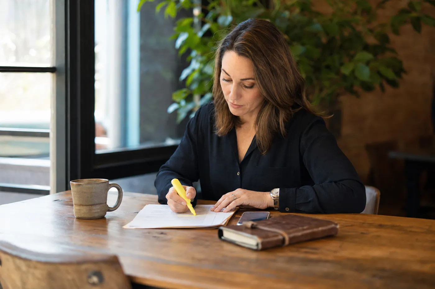 A professional thoughtfully marking a document in a sunlit cafe, representing strategic resume editing for a career pivot.