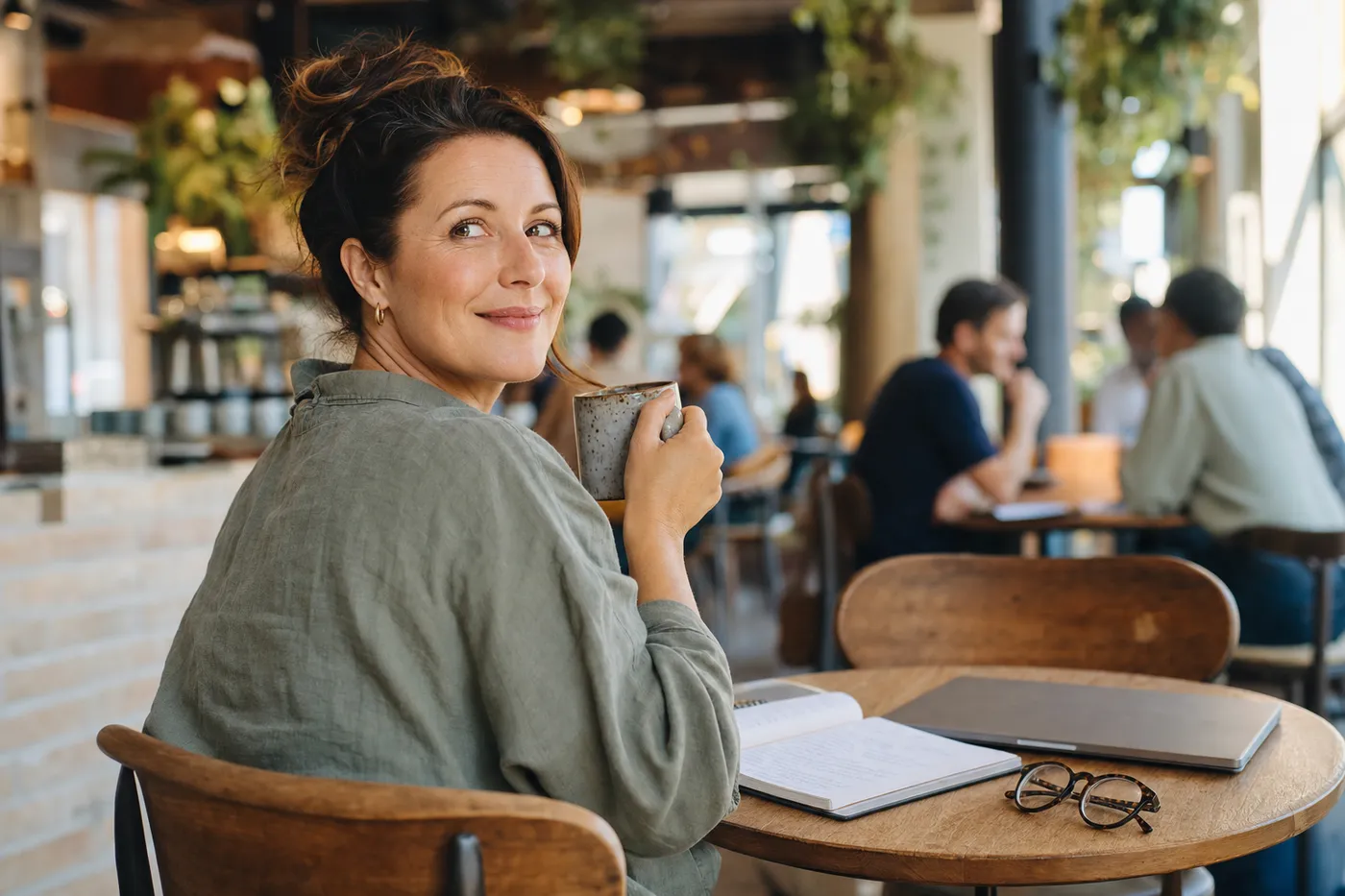 A woman smiles warmly in a sunlit café, reflecting the confidence of starting a successful career transition.