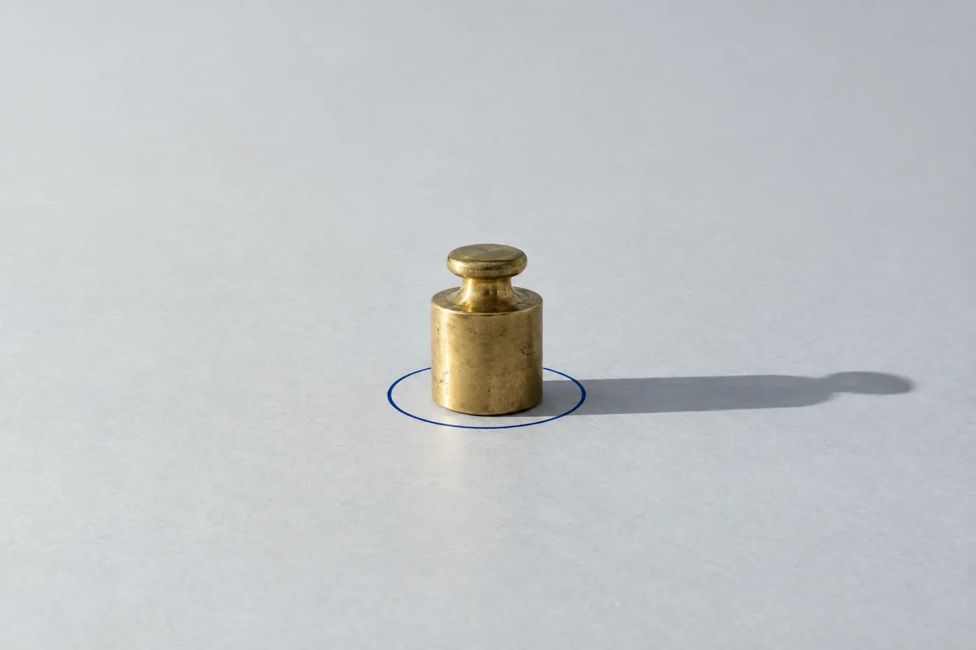 A single brass weight inside a hand-drawn blue circle on a grey desk, representing product prioritization.