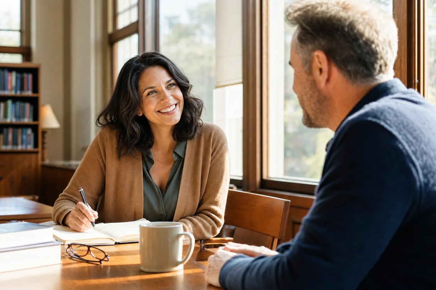 A woman smiles while discussing her career transition notes with a mentor in a sunlit library.