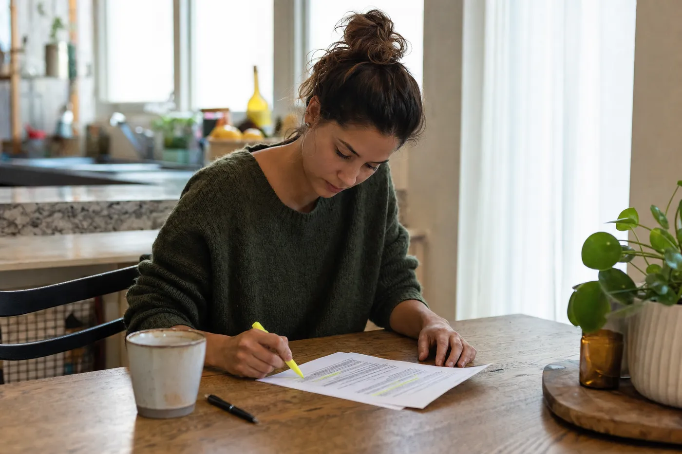 A young woman highlighting key terms on a job description at a sunlit wooden table, preparing her resume.