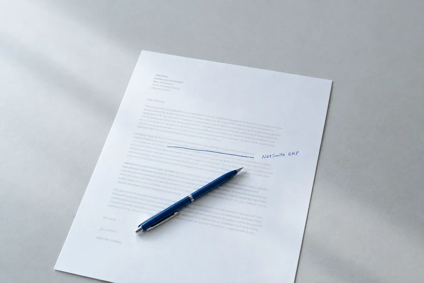 A cover letter draft on a desk with generic text crossed out and 'NetSuite ERP' handwritten in blue ink in the margin.