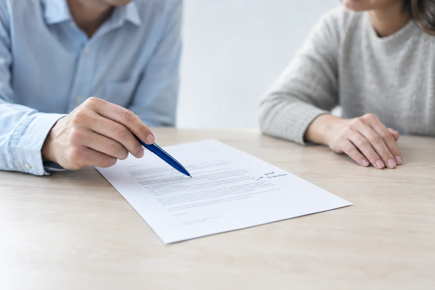 Two people review a printed cover letter on a wood table, pointing to a seamless portfolio reference.
