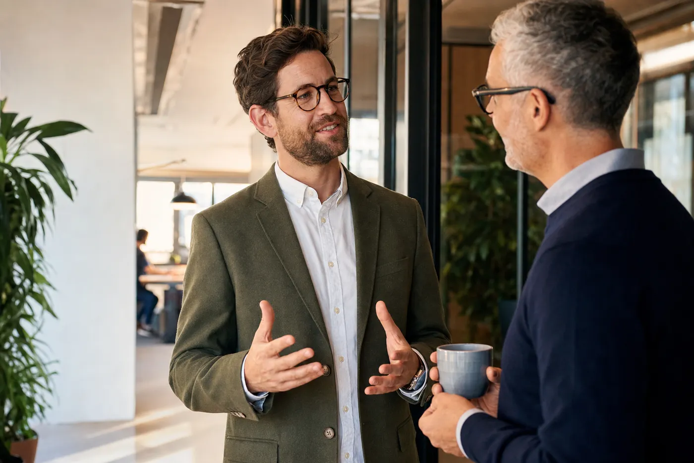 Two colleagues chatting warmly in a sunlit modern office, representing professional familiarity during an internal promotion.