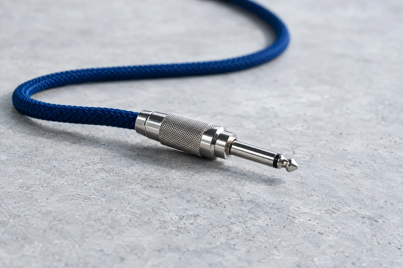 A metal patch cable plug with a blue braided cord on a grey surface, symbolizing connected marketing channels.