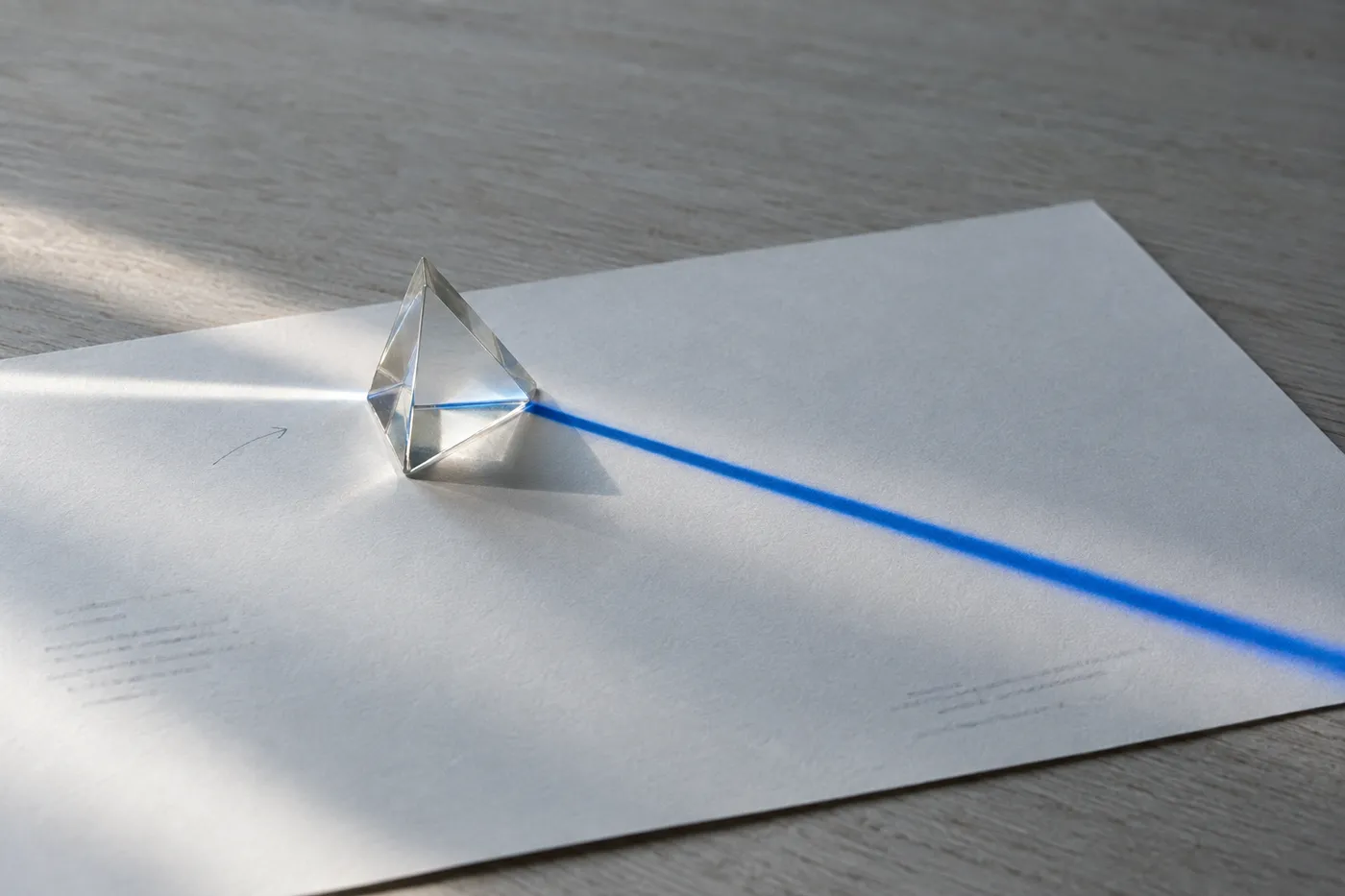 A single glass prism on white paper casting a sharp blue light beam, representing a PM translating effort into clear impact.