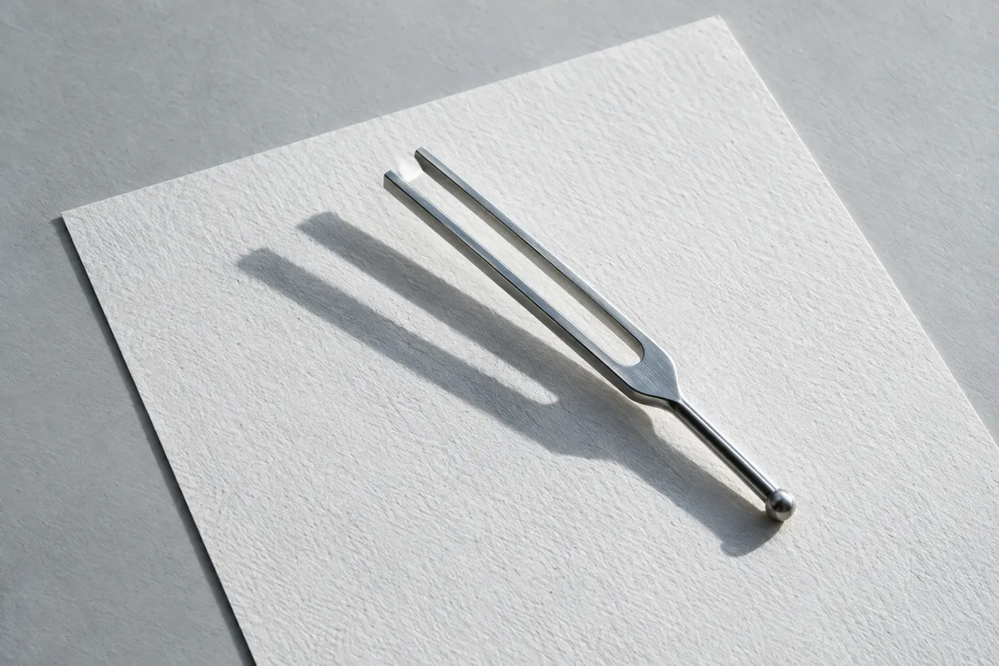 A polished steel tuning fork rests on a blank sheet of white paper, symbolizing setting the right tone in a cover letter.