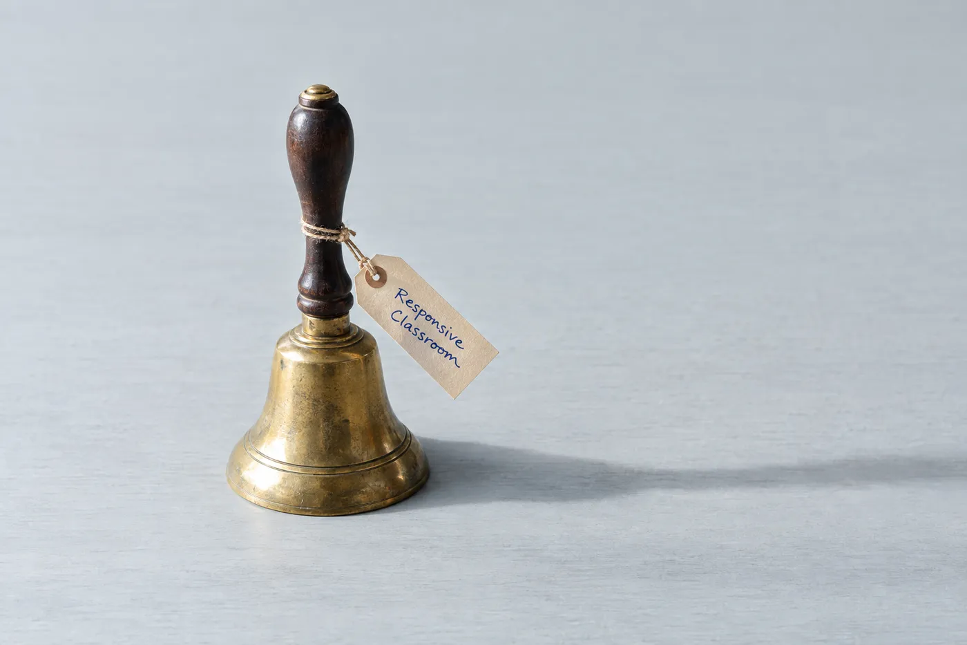 A vintage brass school bell with a handwritten tag reading 'Responsive Classroom' tied to its handle.