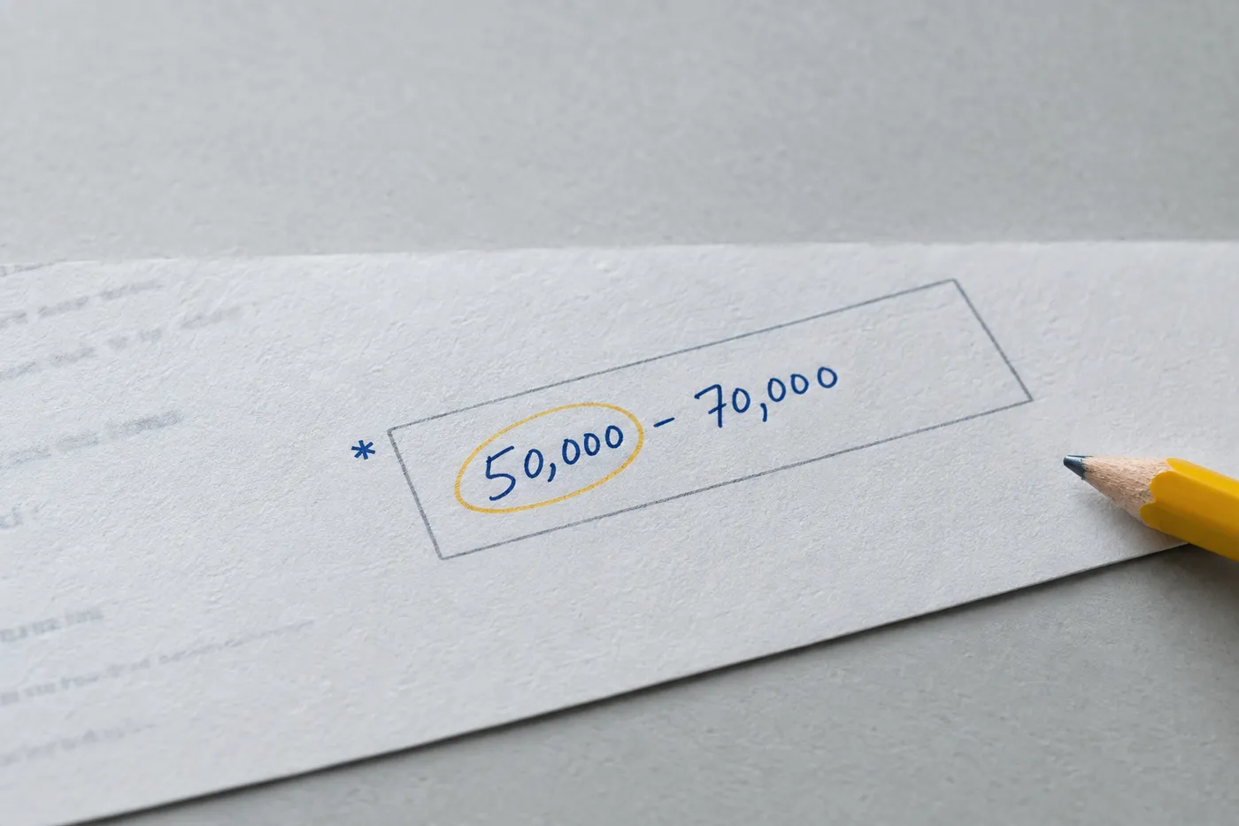 Close-up of a paper application's required salary field filled in with a handwritten range, highlighting the minimum.