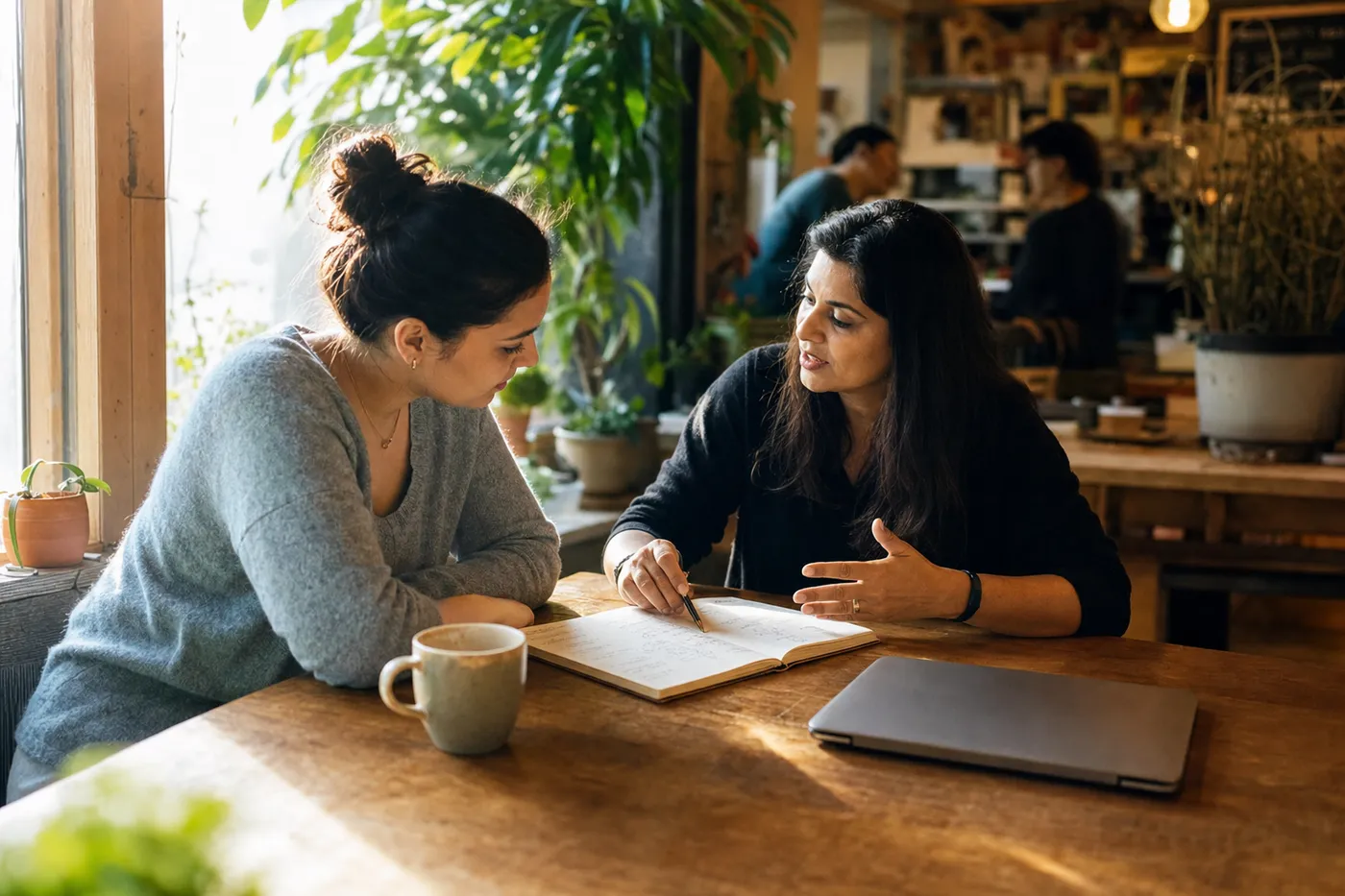 A candidate and mentor discuss career strategy in a bright cafe, learning how to stand out as a bootcamp graduate.