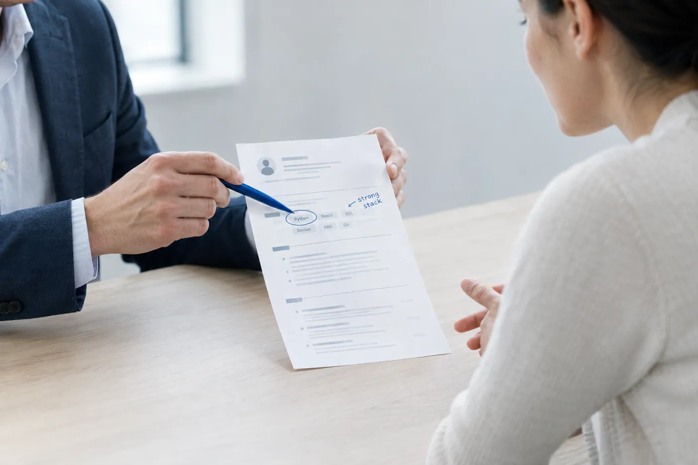 An interviewer points to a circled technical skill on a candidate's resume during an Android developer interview.