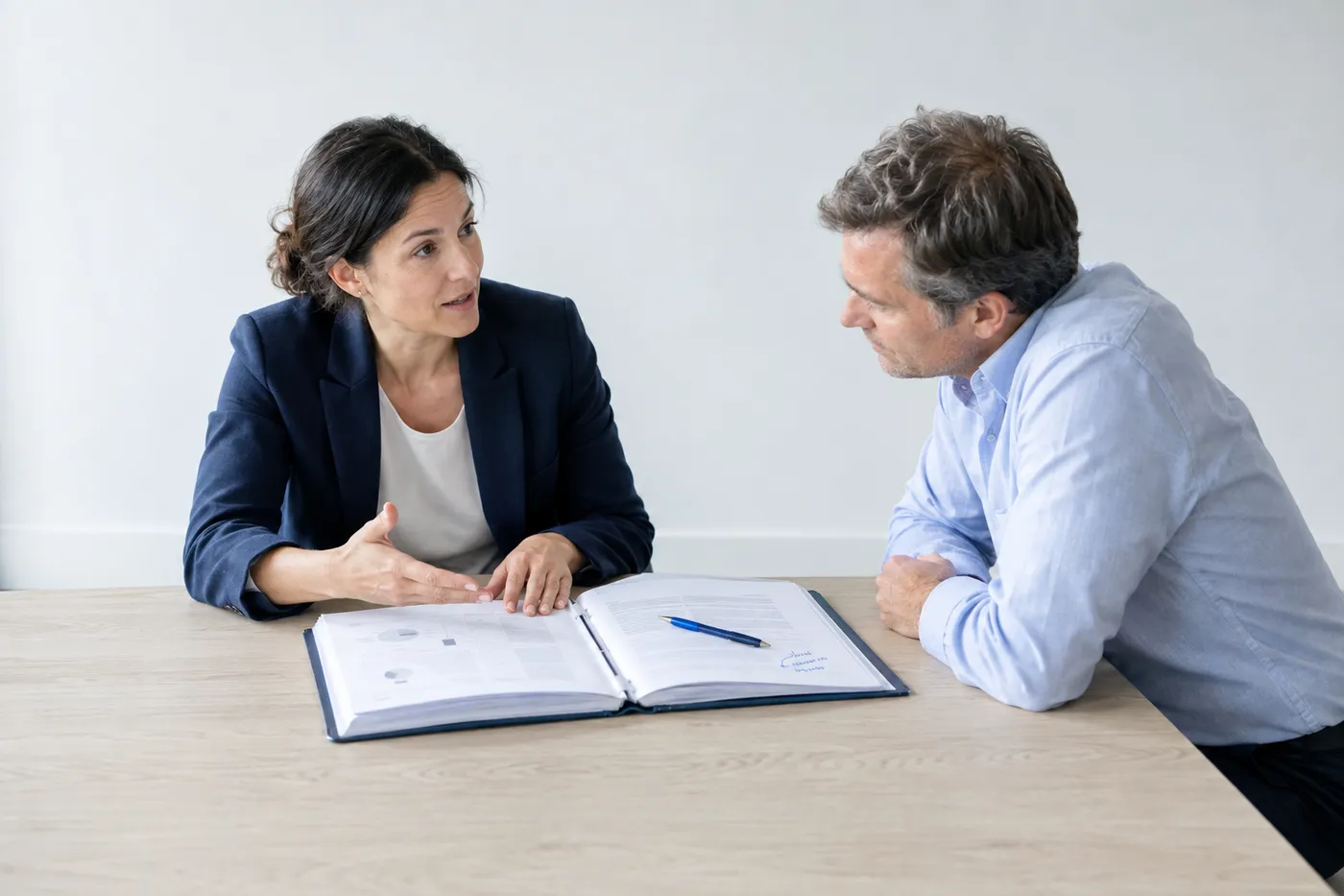 Two people at a conference table discussing a thick document binder, representing board-level strategic communication.