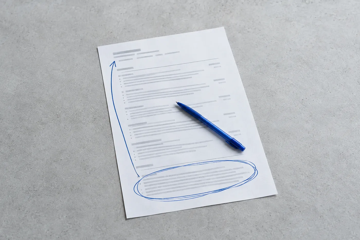 A printed resume on a grey desk with a hand-drawn blue arrow pointing from a circled section at the bottom to the top.