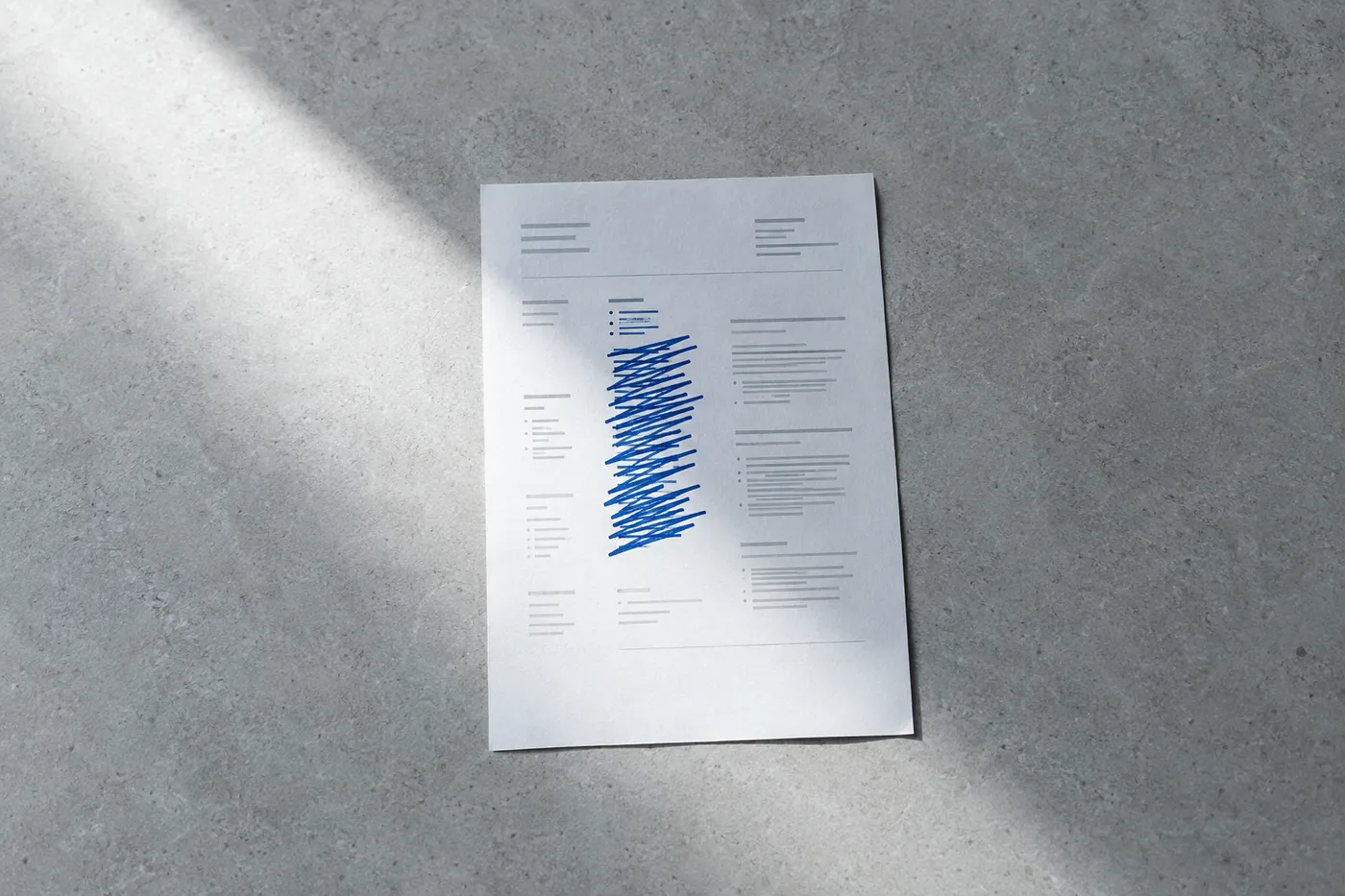 A single printed resume on a grey desk, with a long list of skills crossed out in blue ink except for three core items.