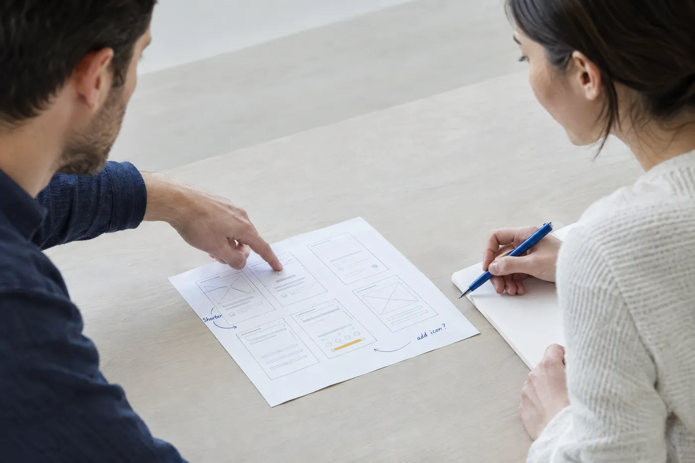 A product designer takes notes during a paper-prototype usability test with a participant.
