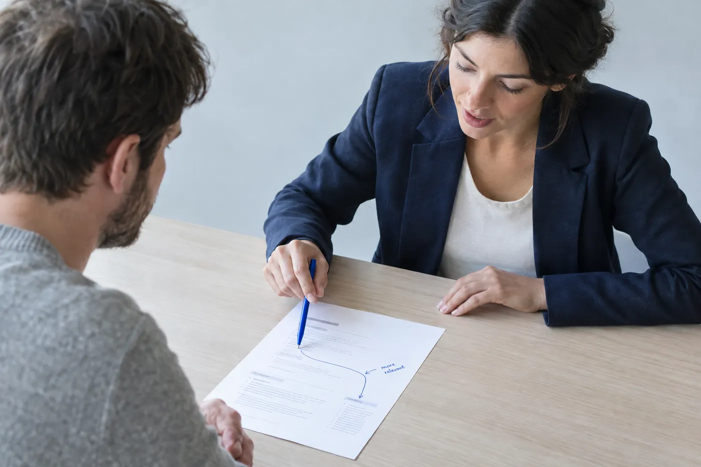 A candidate uses a blue pen to bridge a gap on a resume during an interview, explaining their career transition.