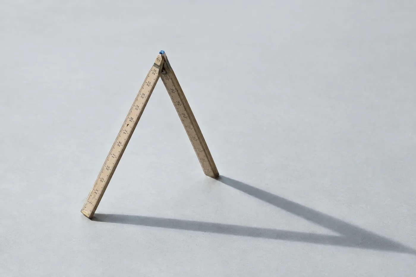 A wooden folding ruler standing on its edge in a sharp triangle shape on a grey desk, symbolizing a project milestone.