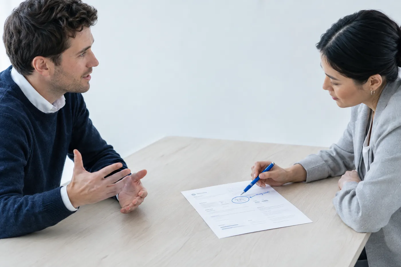 Two professionals in an interview, with the interviewer focusing on a circled metric in the top summary of a printed resume.