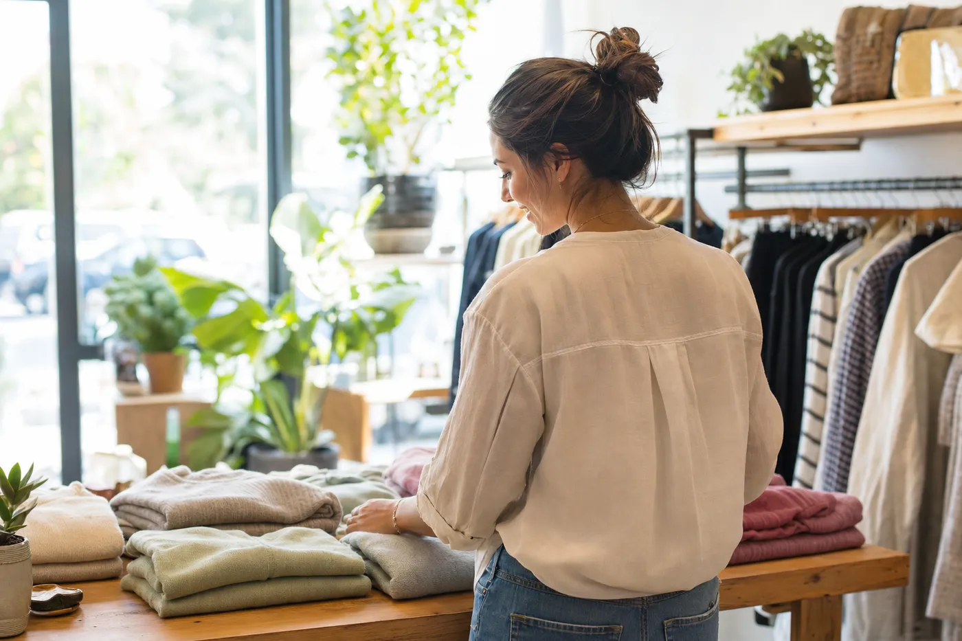 A smiling retail associate arranging a clothing display in a bright, modern boutique, representing customer service excellence.