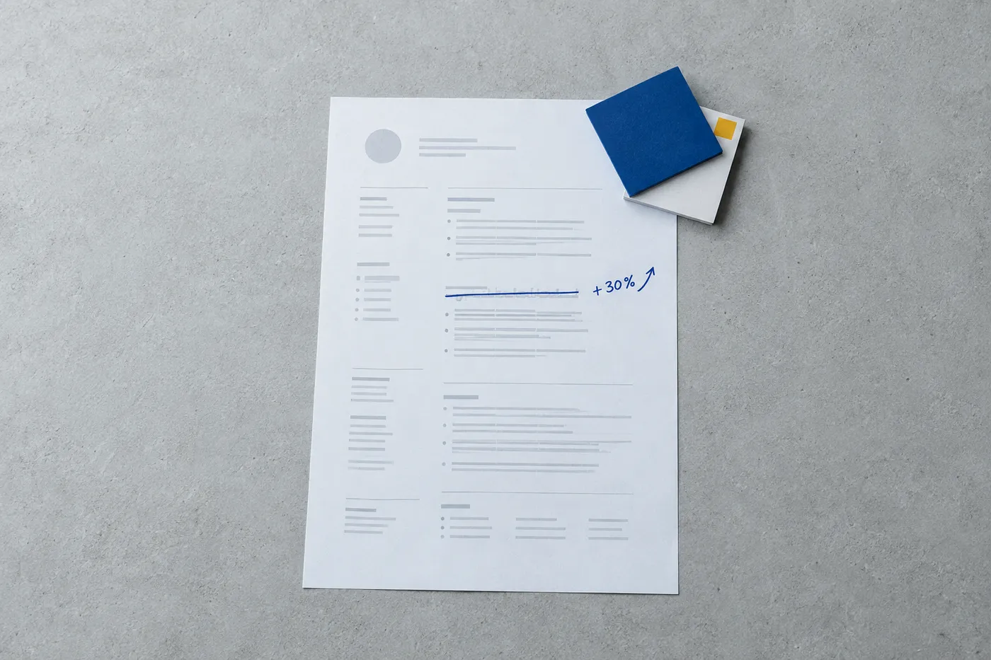 A flat-lay view of a resume where a generic bullet point is crossed out in blue ink and replaced with a handwritten metric, beside two certification cards.