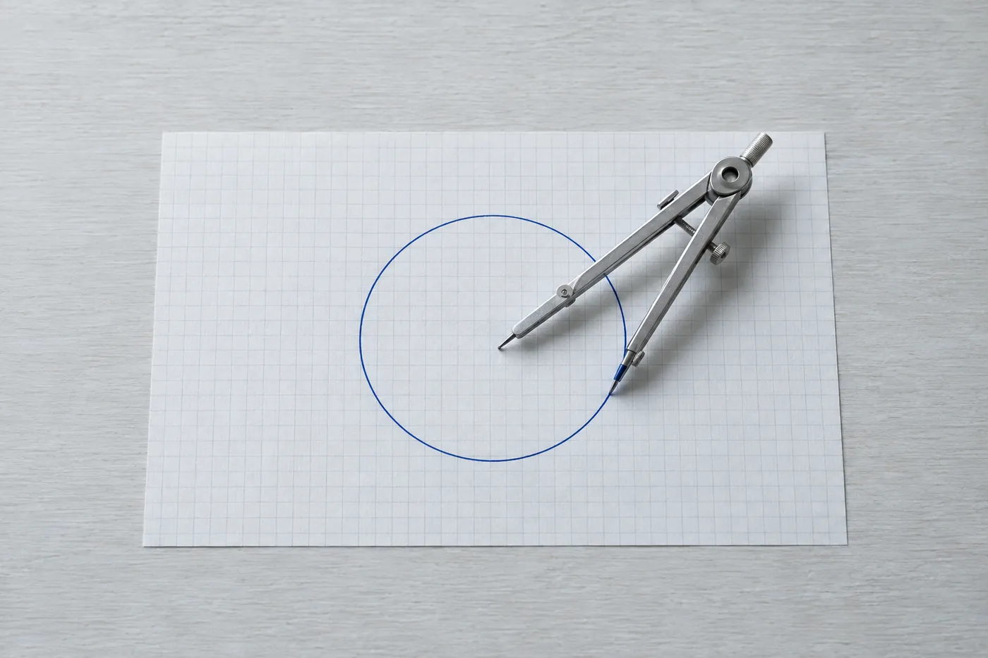 A metal drafting compass on grid paper beside a perfect circle drawn in blue ink, representing system lifecycle design.