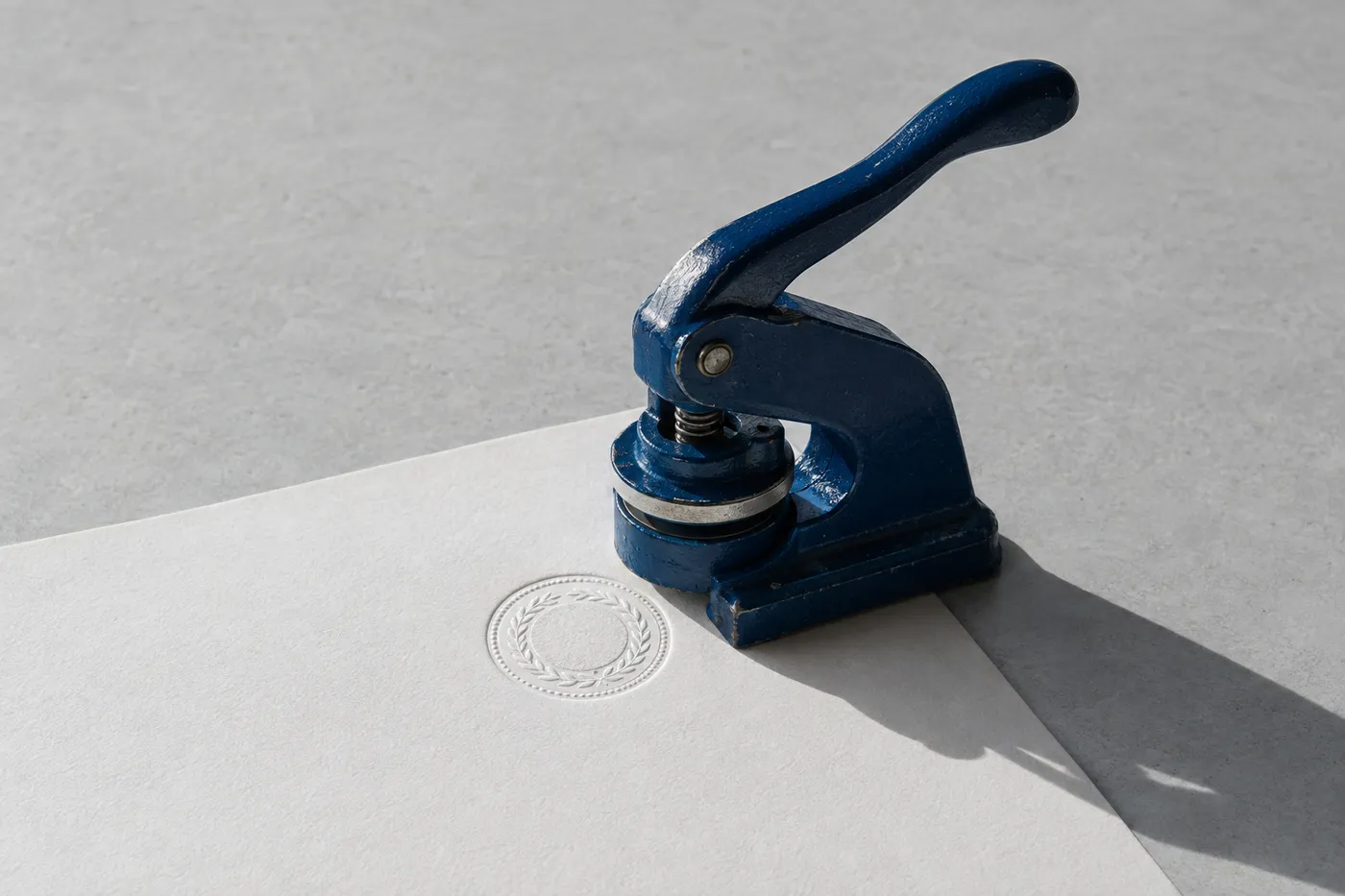 A heavy blue metal embossing press on a sheet of white paper, showcasing a raised official certification seal.